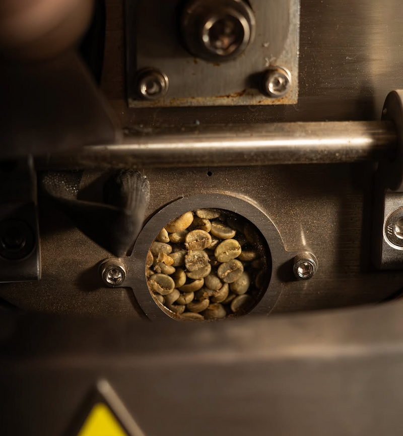 Coffee beans roasting and browning inside the sight glass of a small-batch coffee roasting machine in Mysore.